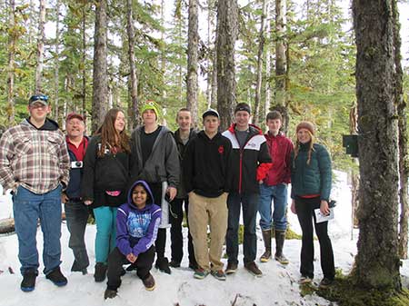 Highschool age citizen scientists in Gustavus Kohan is on the right and a bat detector is mounted to a tree next to her Science teacher Eric Hart is second from left These volunteers will monitor this site in Glacier Bay National Park over the summer
