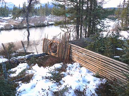 The basket style tazrsquoin fi sh trap and fence constructed of spruce slats and used by Lime Village residents to harvest least cisco at Shagelagh during 2013 After use the fish trap and fence were removed from the water and stored on the shore of Hungry Creek Photo by James M Van Lanemen em